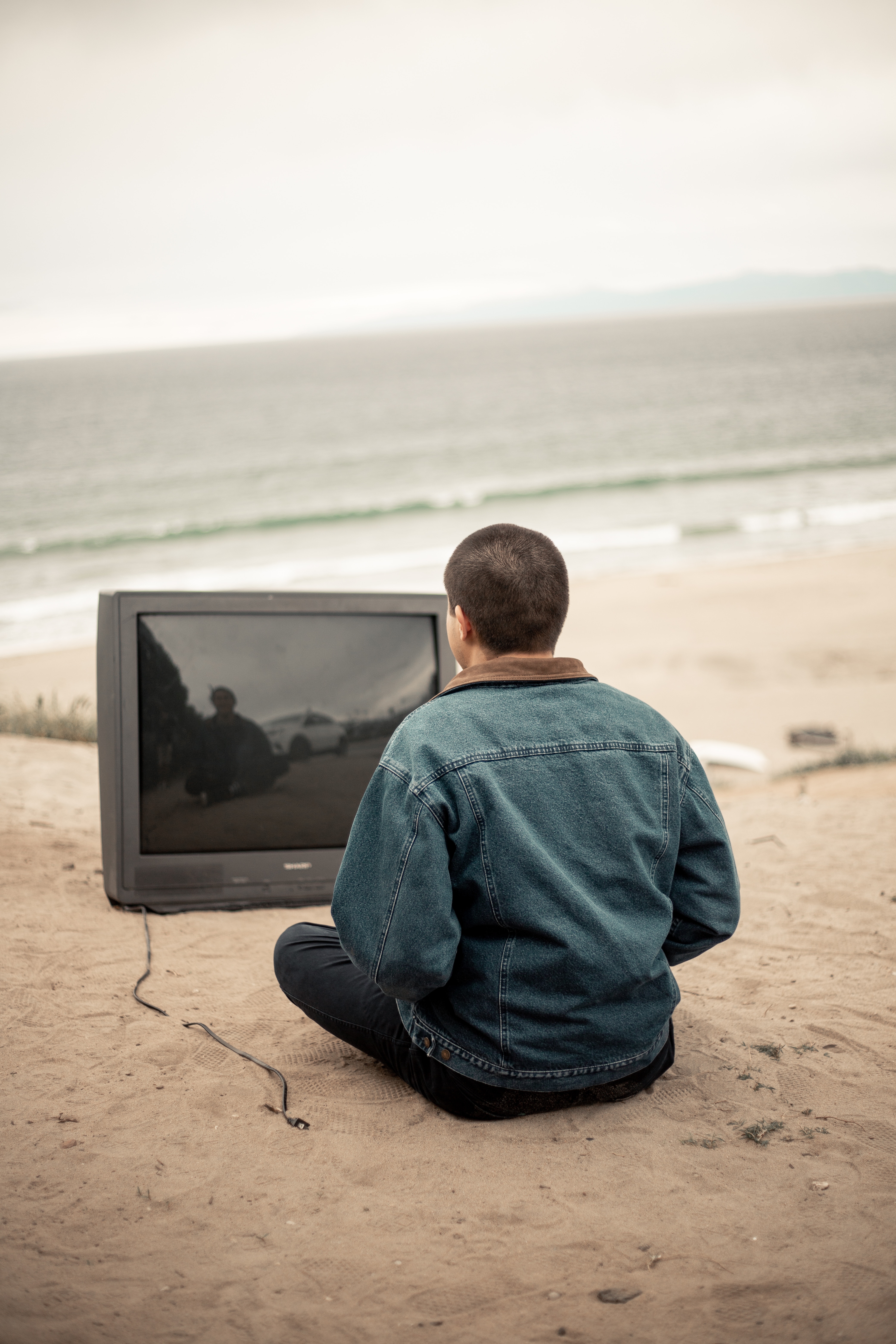 Man sitting on beach staring at an old tv.